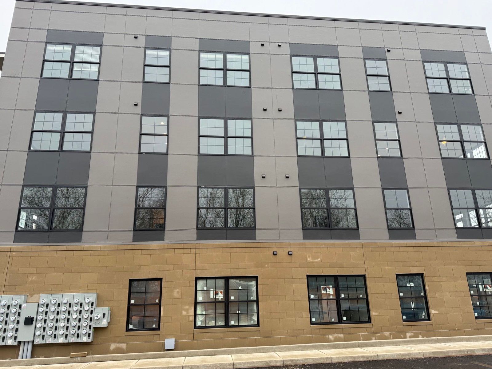Modern four-story building with gray upper facade, tan brick lower level, and rows of windows