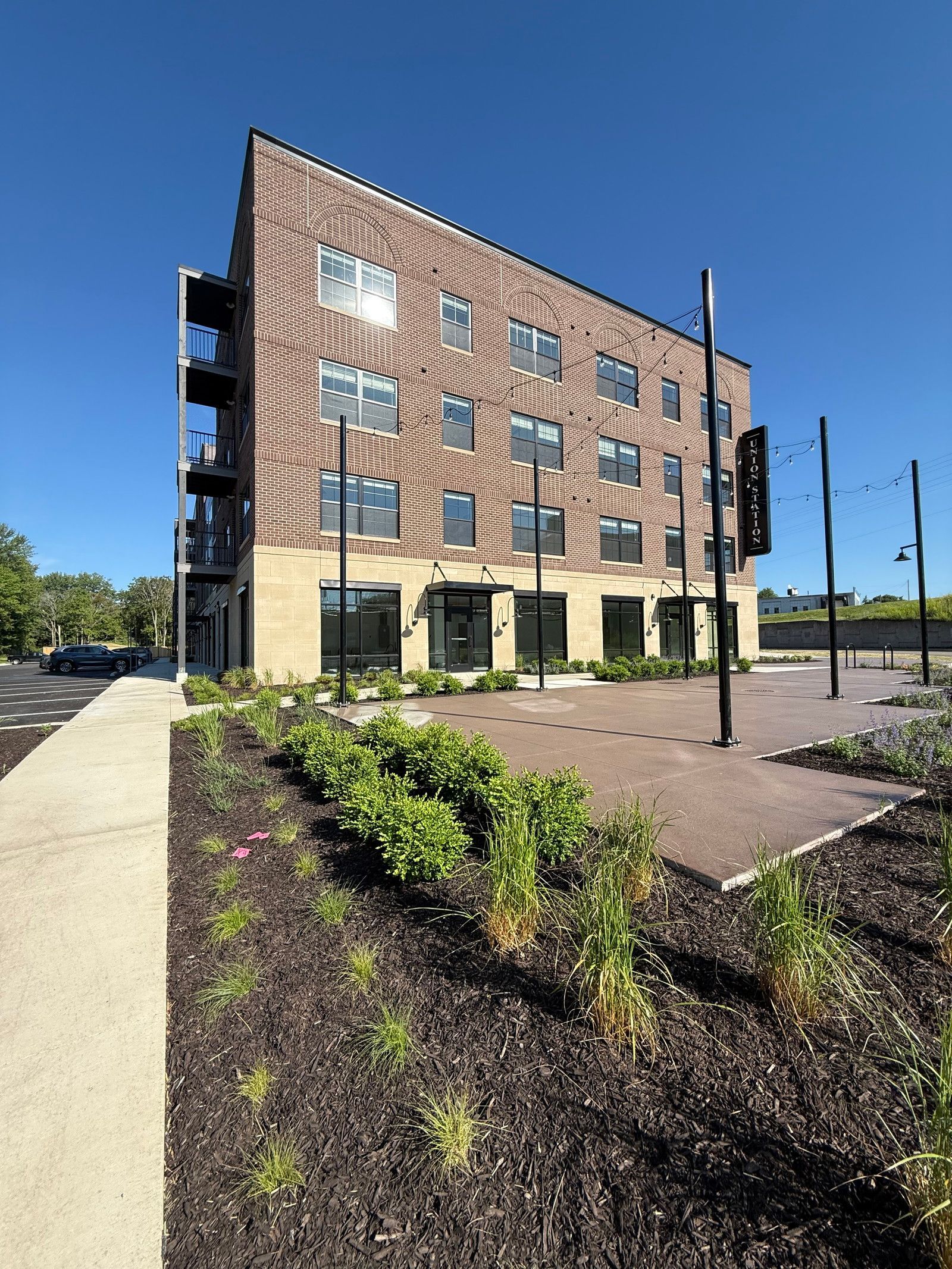 Modern brick apartment building with balconies and landscaped walkway under a clear blue sky