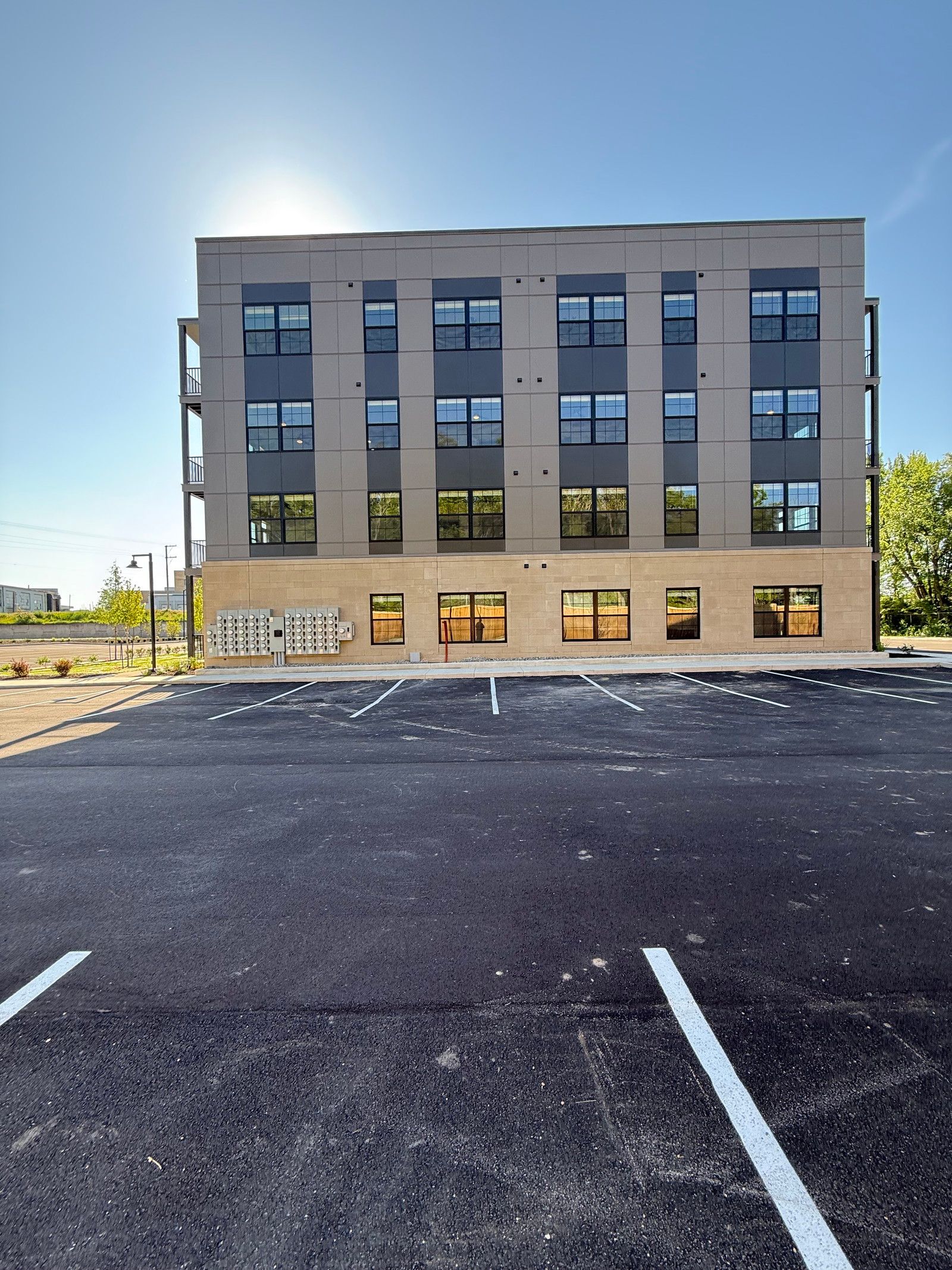 Modern four-story building beside an empty gravel parking lot under a clear sky.