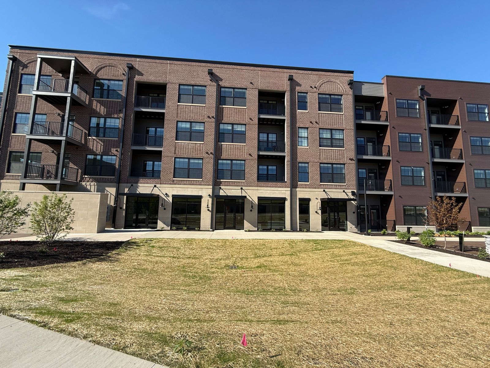 Brick apartment building with balconies and a grassy courtyard under a blue sky