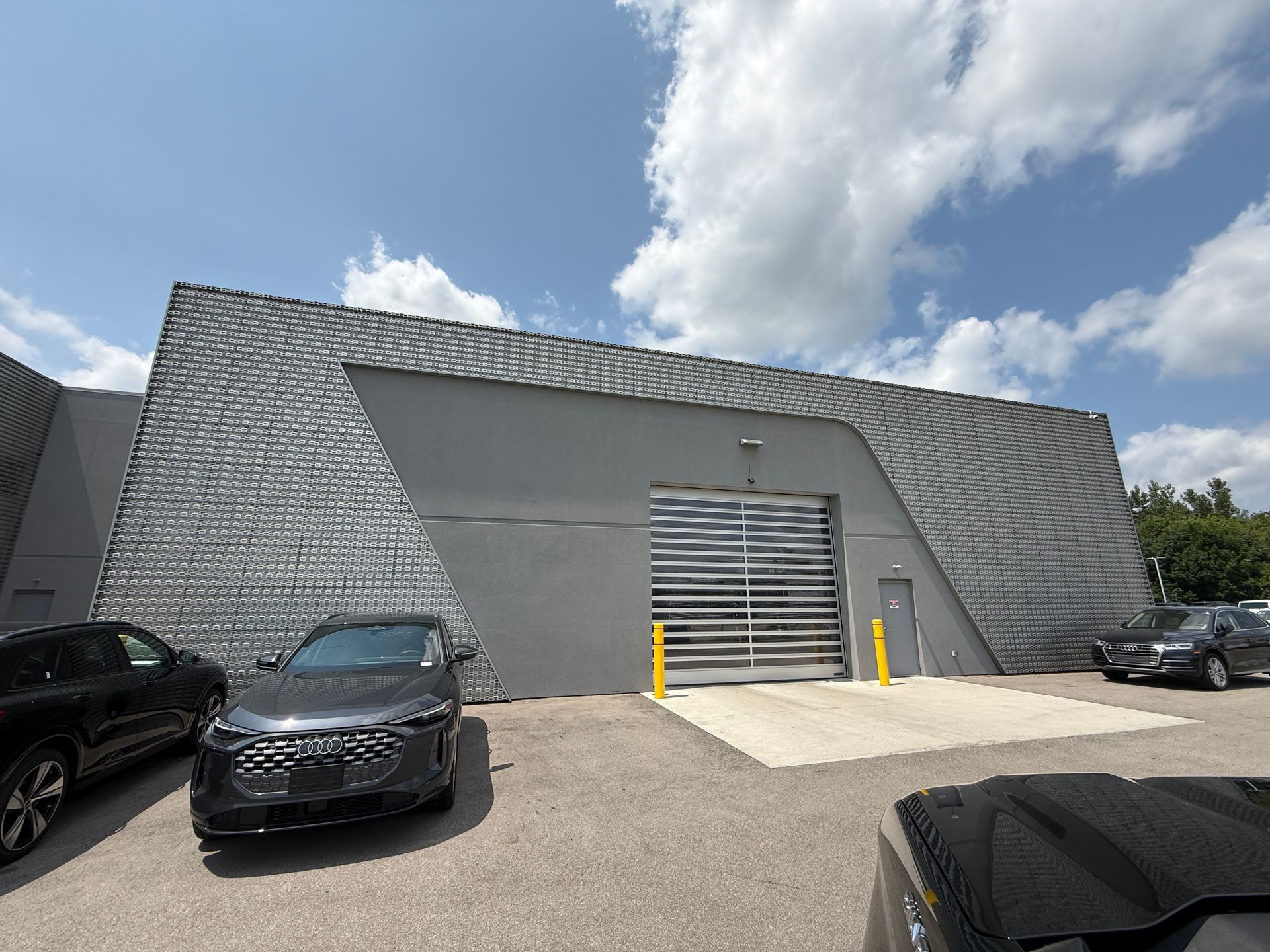 Industrial building with metal façade, loading door, and parked cars under a cloudy sky