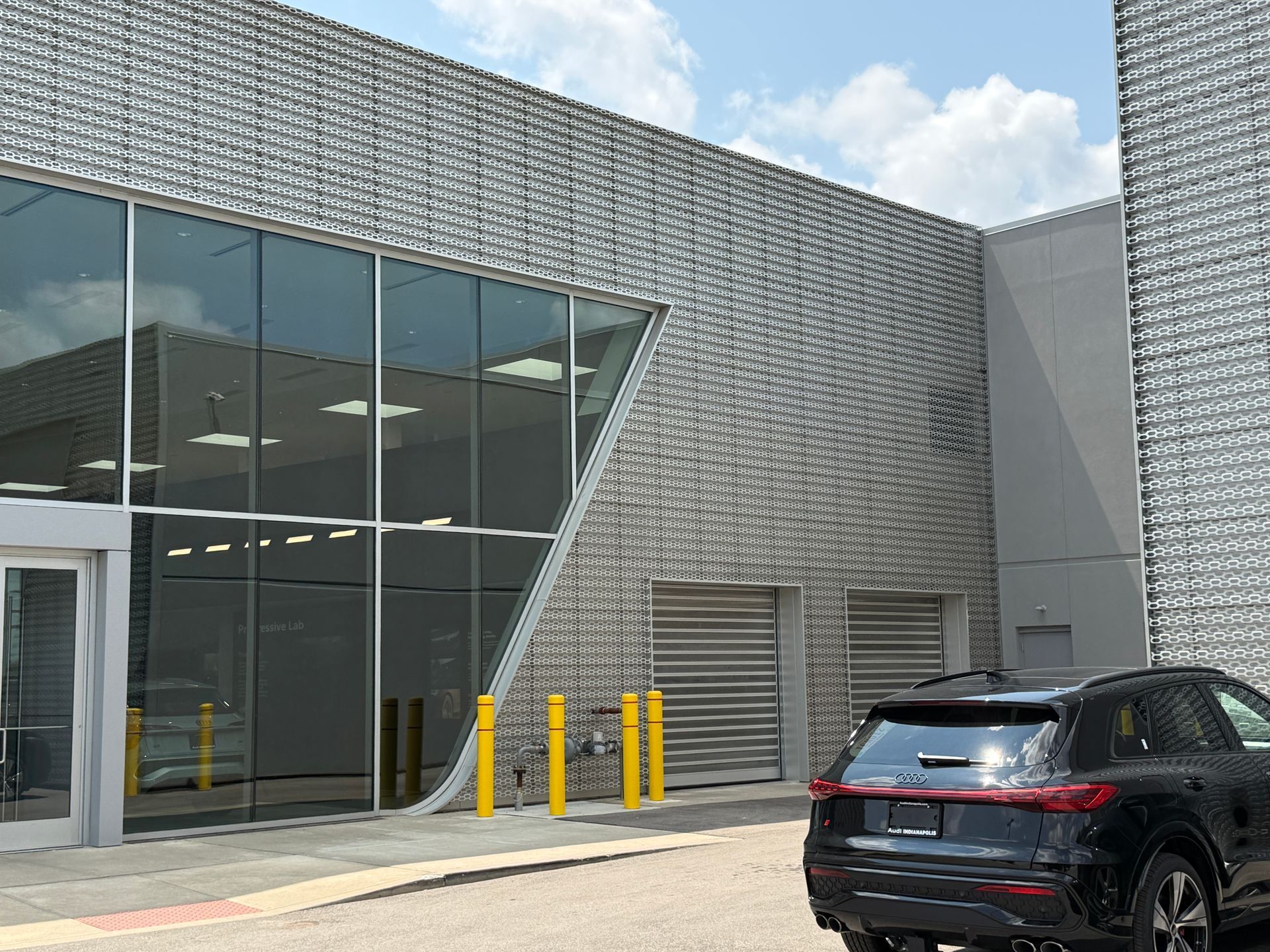 Modern building exterior with large glass windows, yellow bollards, and a black SUV parked outside