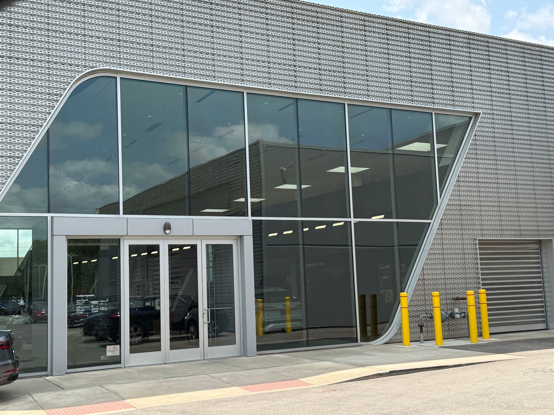Modern building entrance with large slanted glass windows and yellow bollards