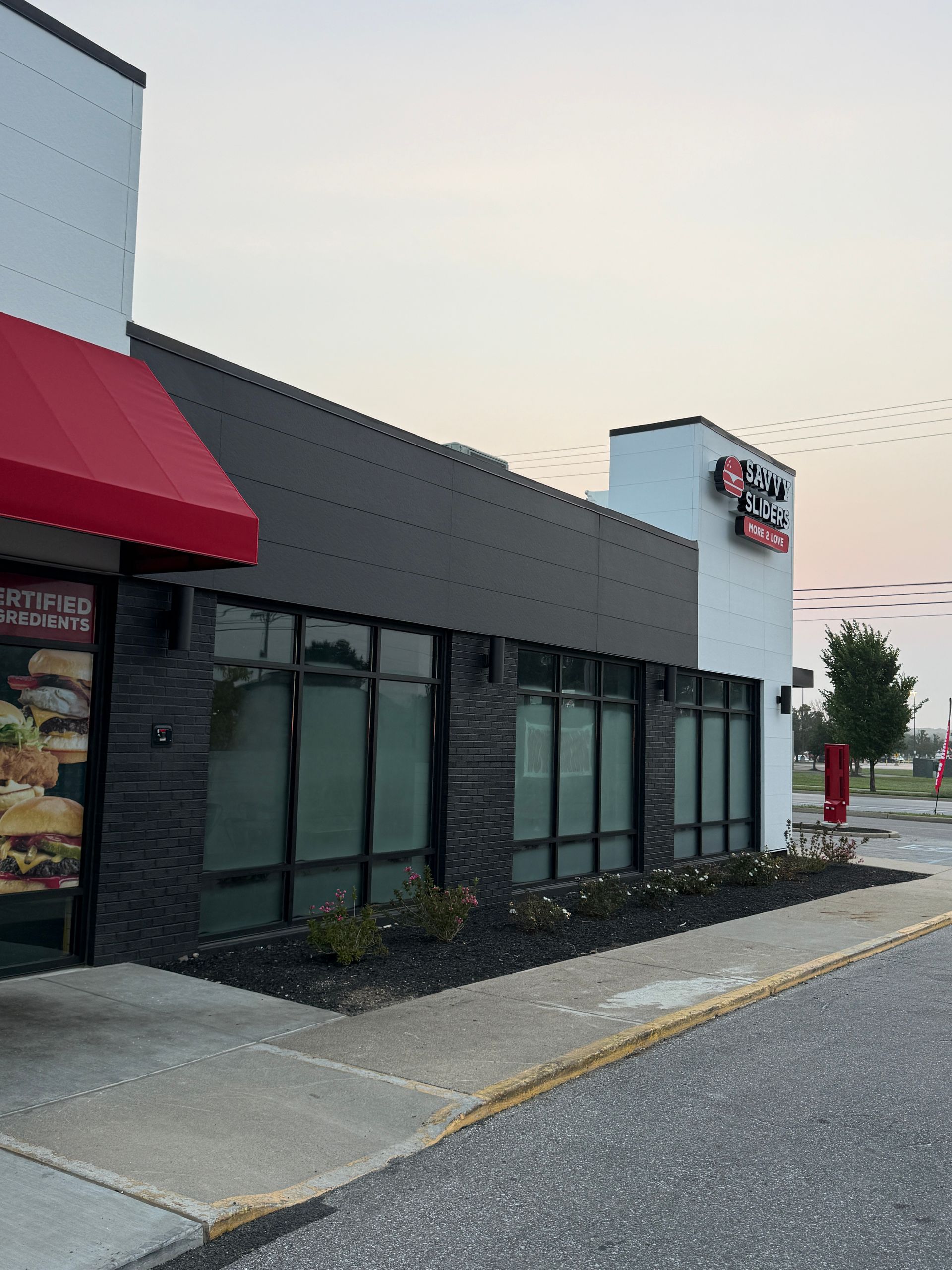 Exterior of a strip mall storefront with dark windows, red awning, and parking lot at dusk