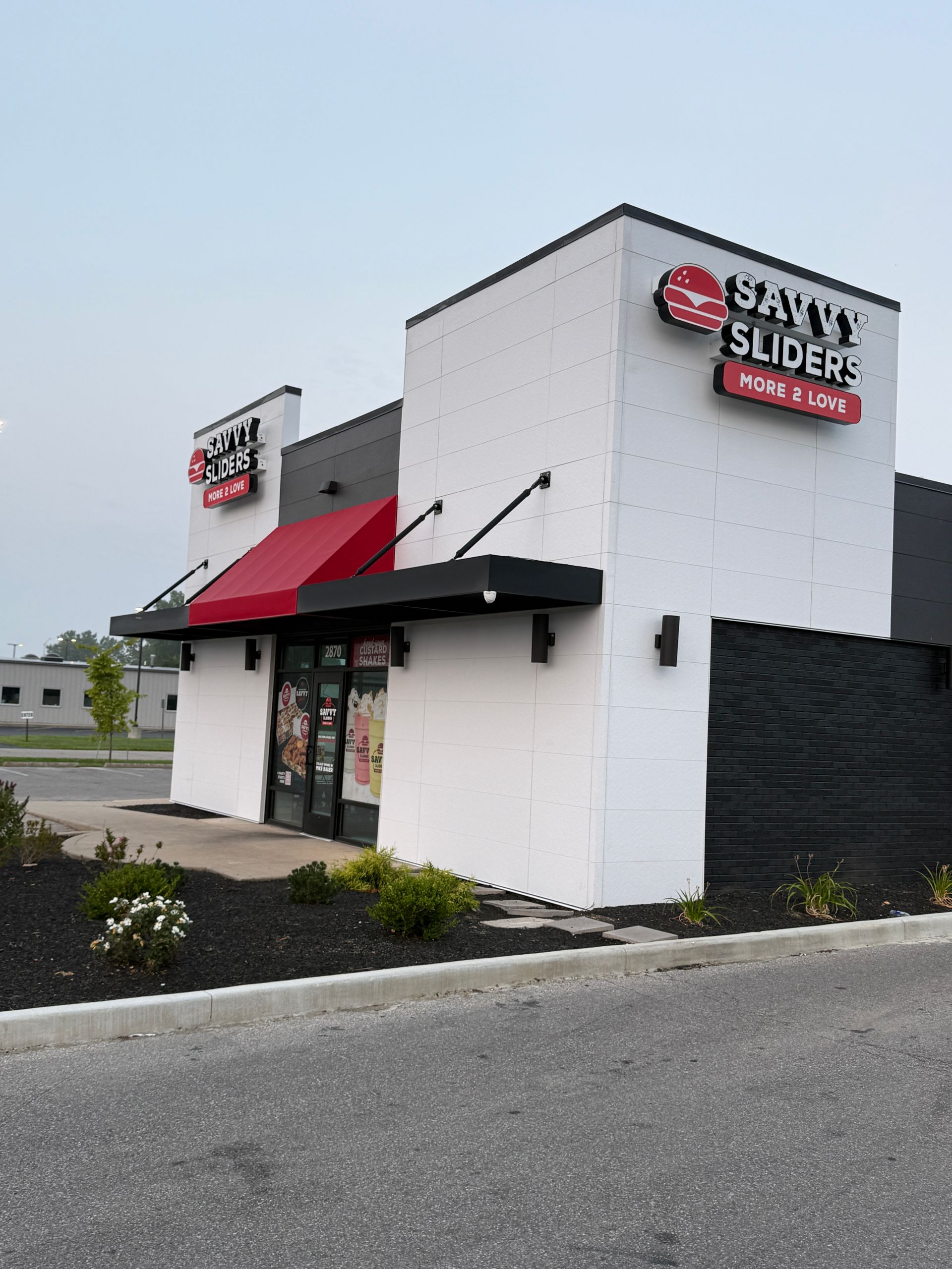 Corner view of a white sandwich shop with red awnings and a black side wall in a parking lot