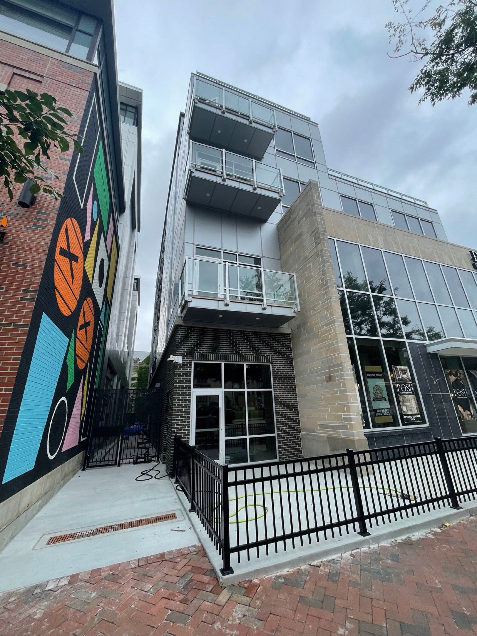 Modern multi-story building with glass windows, white exterior, and a colorful mural on the side, viewed from the sidewalk.