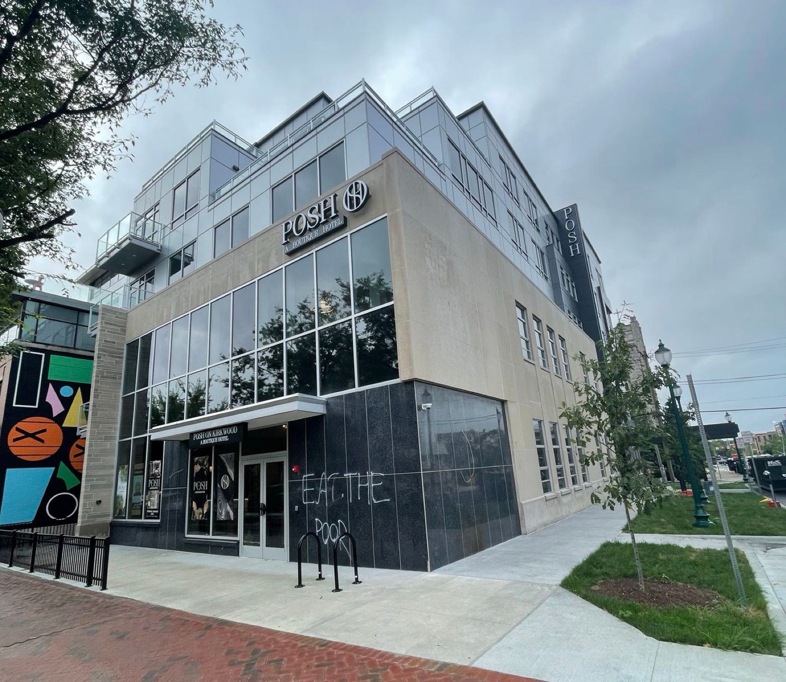Modern gray-and-white corner storefront with large windows, black entrance, and sidewalk under cloudy sky