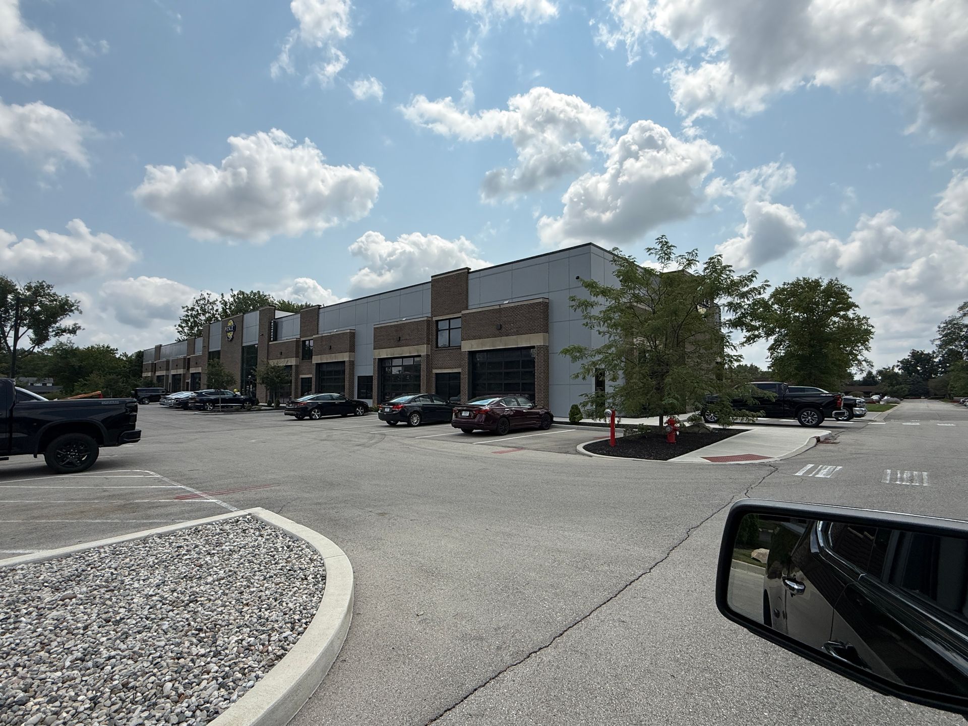 Strip mall parking lot with storefronts, parked cars, and a cloudy sky