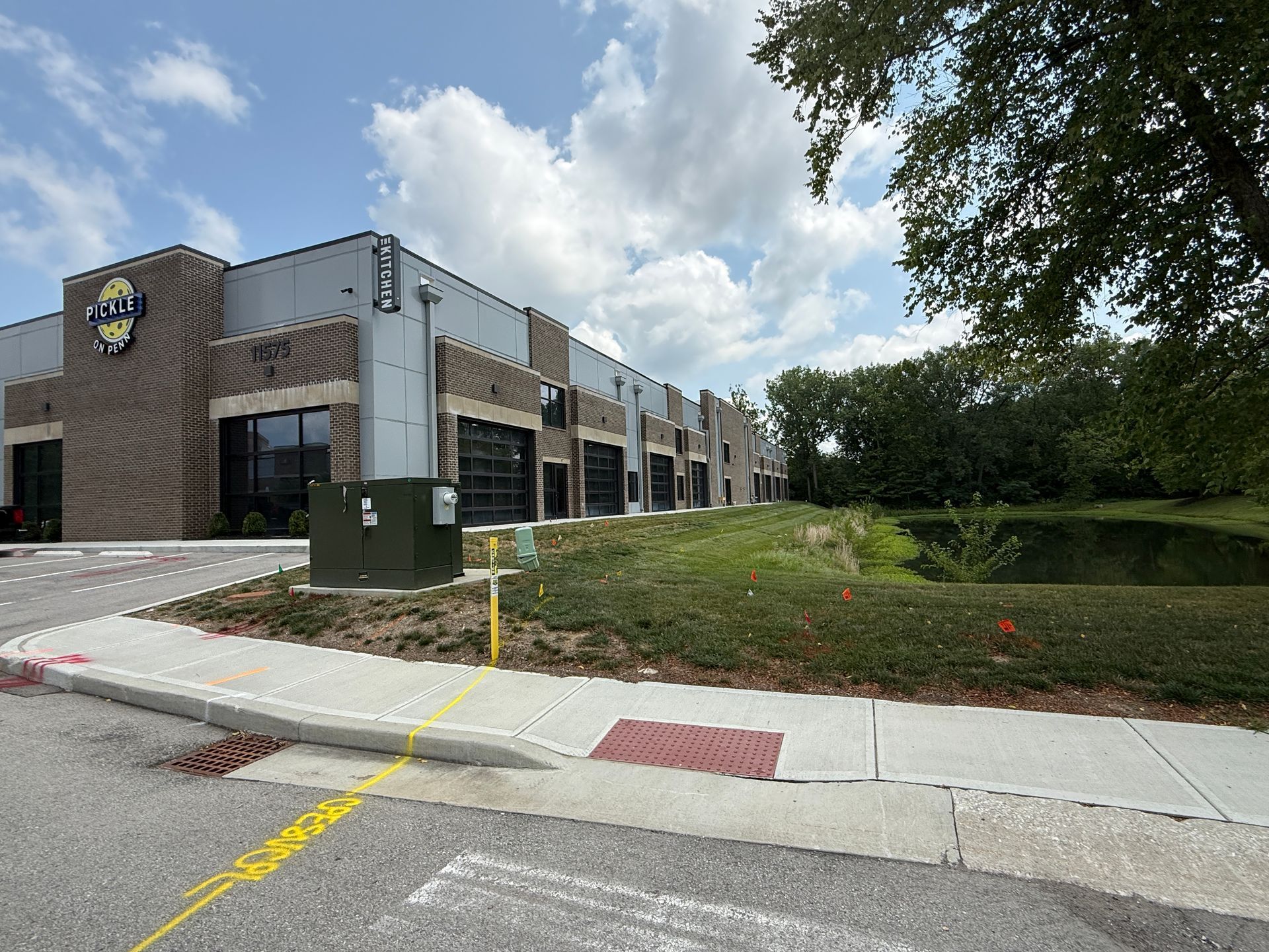 Modern office building with parking lot, grassy slope, and trees under a partly cloudy sky