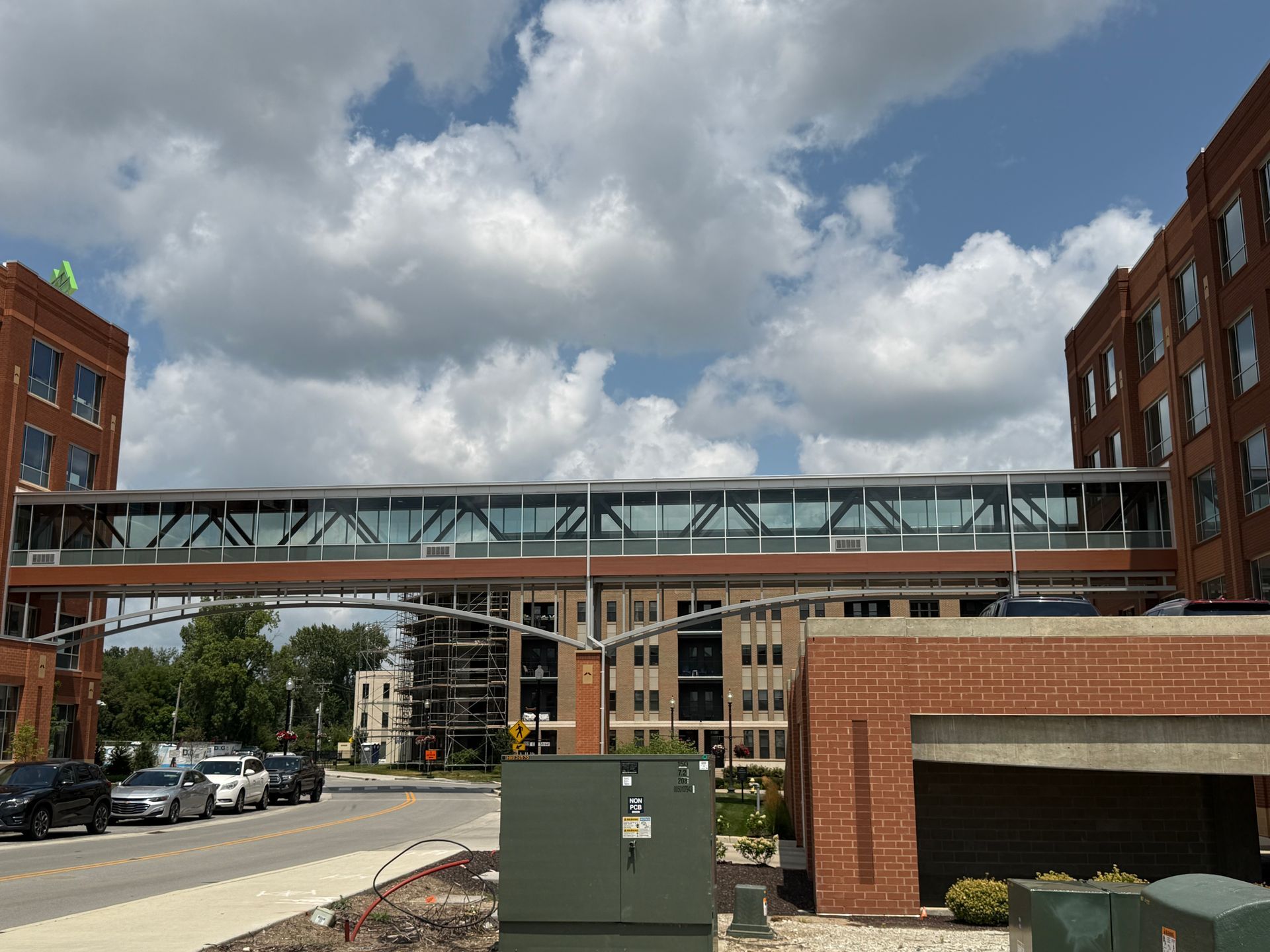 Brick buildings linked by a glass skybridge over a street under a cloudy sky.