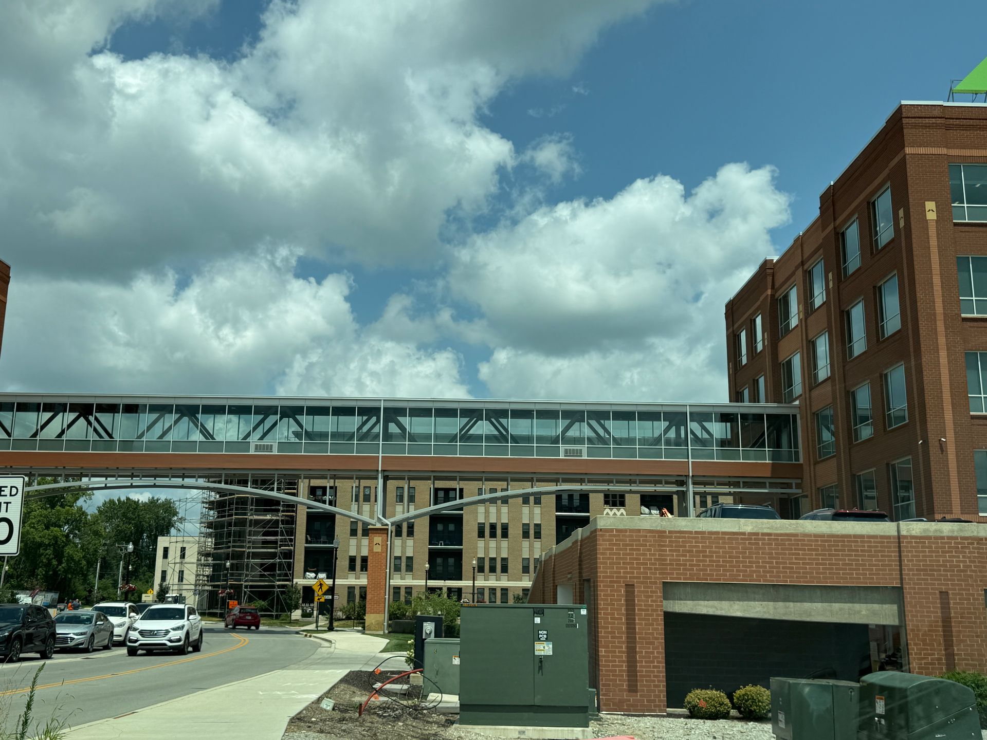 Urban street with a skybridge linking brick buildings under a cloudy blue sky.