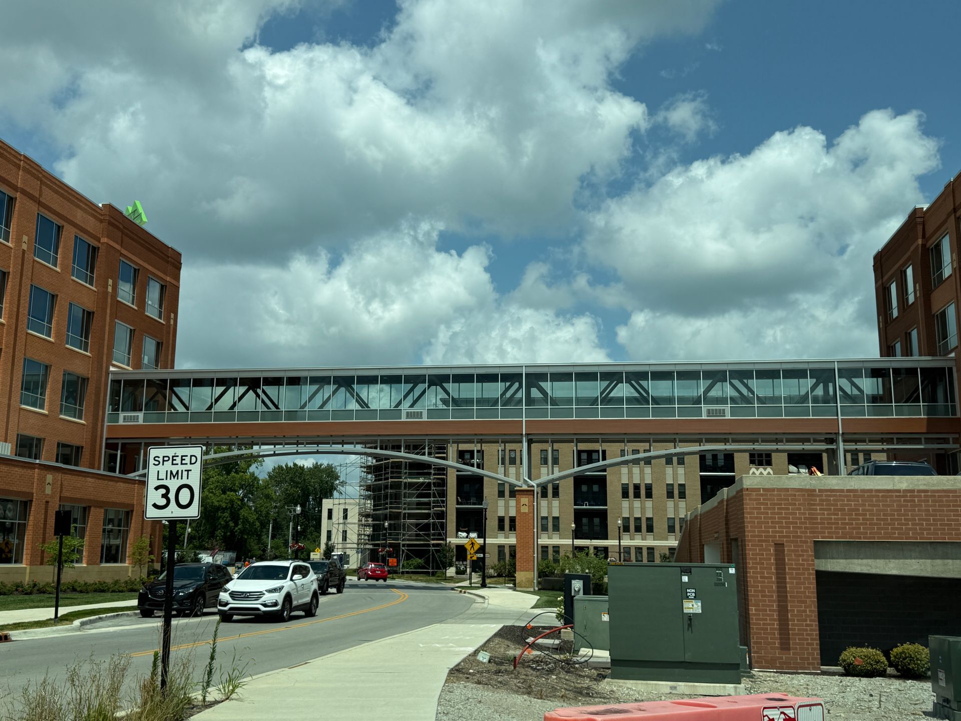 Urban street with a pedestrian skybridge between brick buildings under a cloudy sky, cars below.