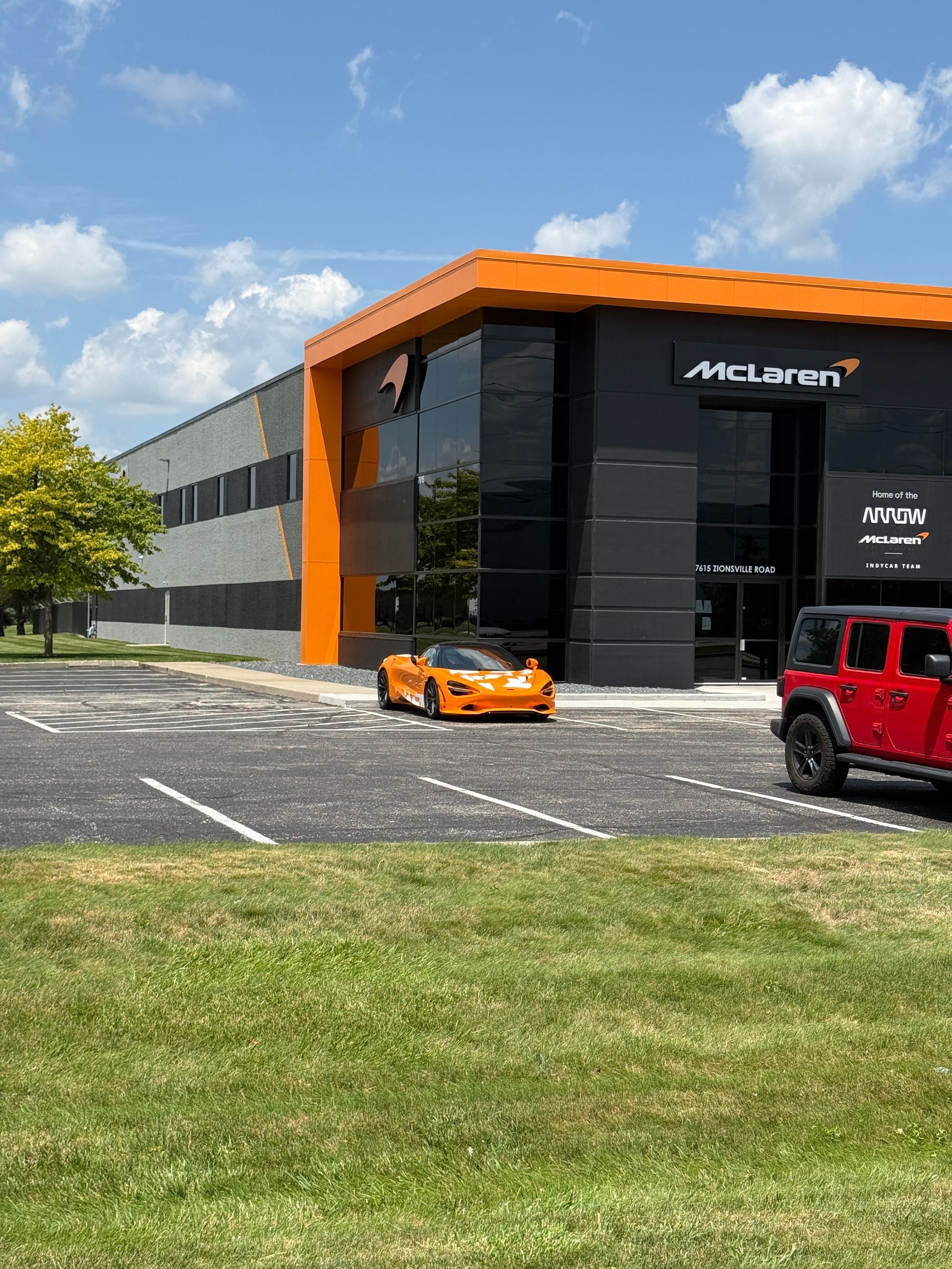 McLaren dealership with an orange sports car parked outside and a red SUV nearby