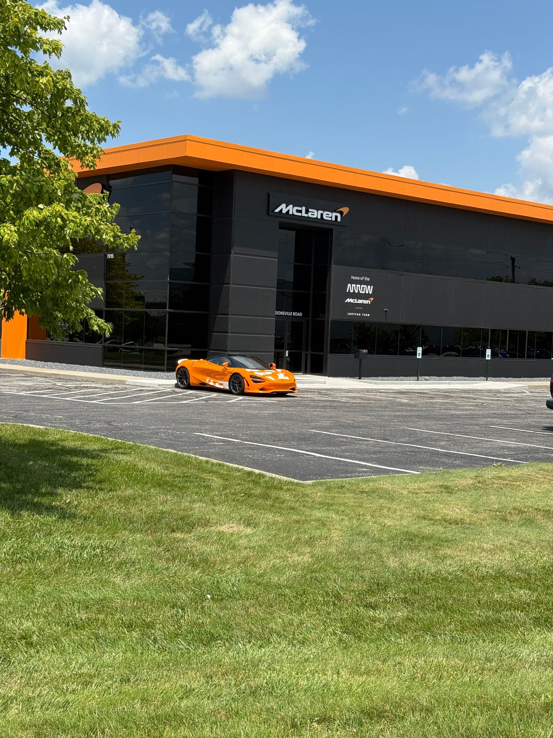 Orange sports car outside a black McLaren showroom under a bright sky