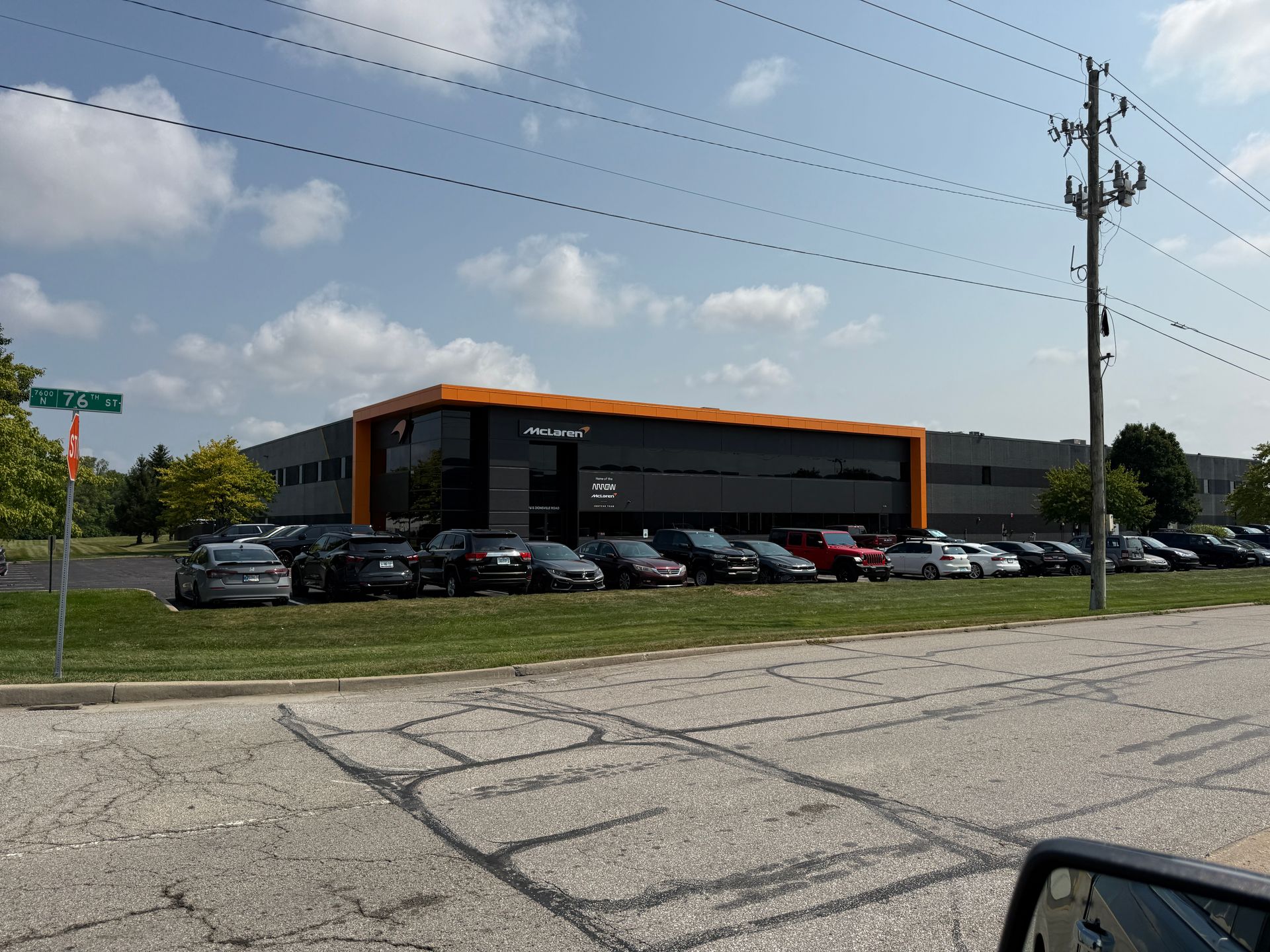 Street view of a modern black-and-orange commercial building with parked cars under a cloudy sky.