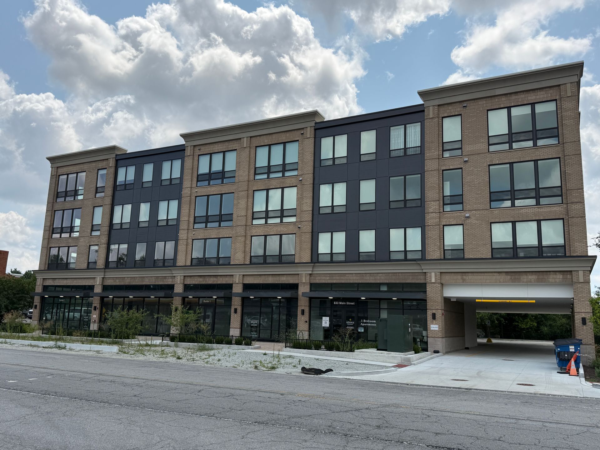 Five-story brick apartment building with large windows and ground-floor shops under a cloudy sky.
