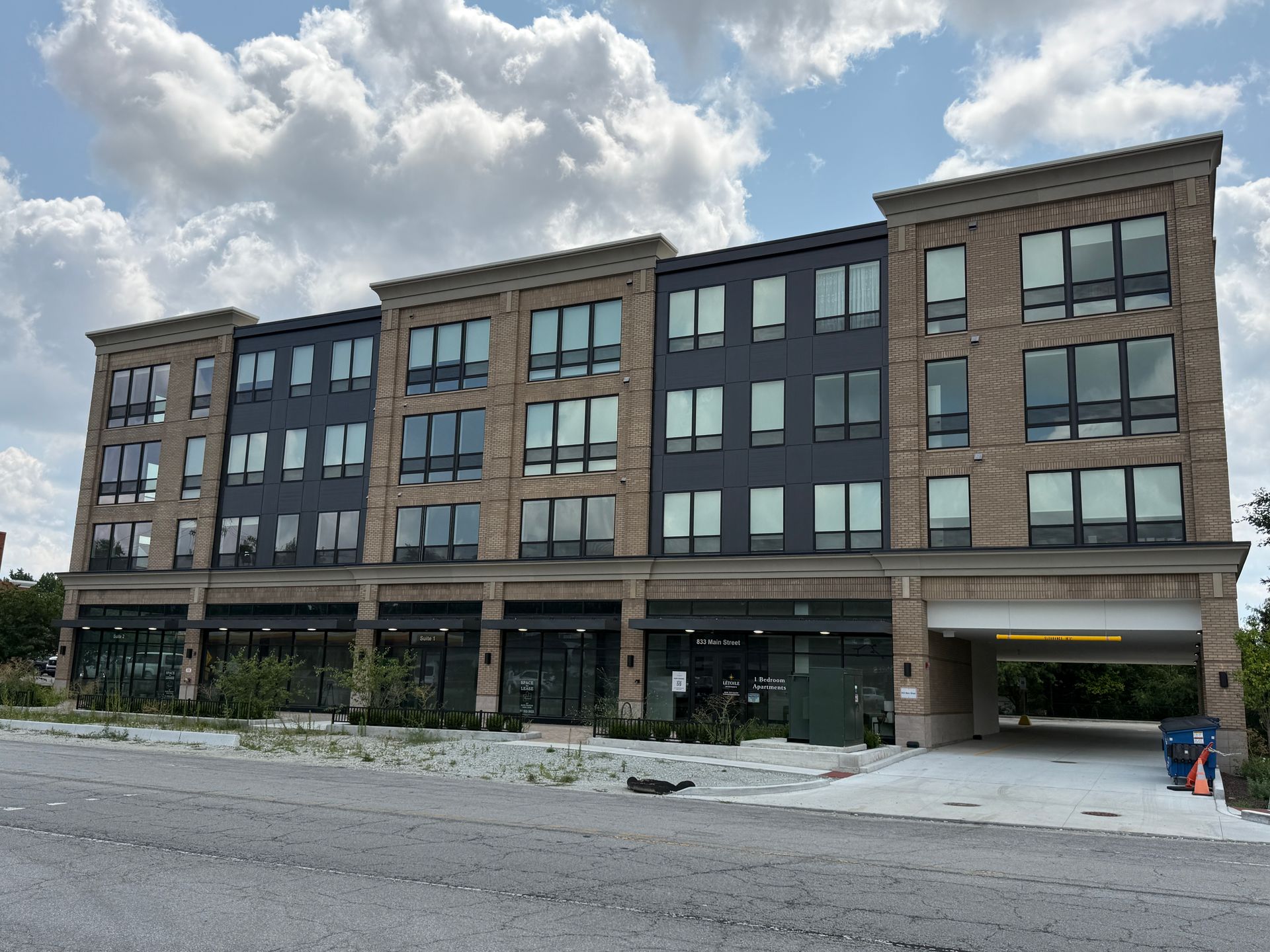 Modern four-story brick-and-glass apartment building with ground-floor storefronts under a cloudy sky
