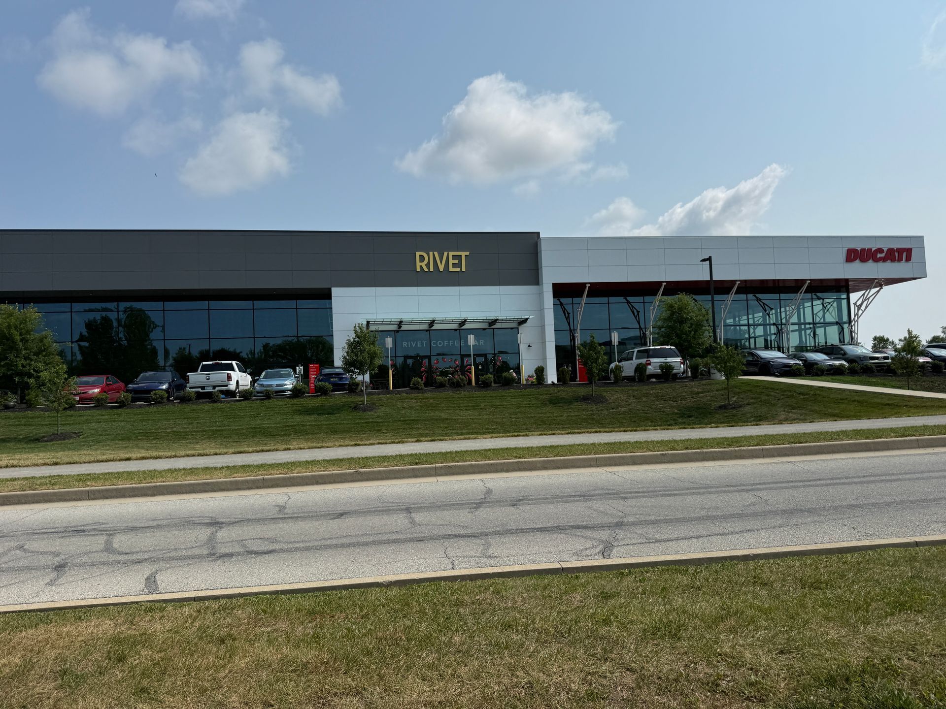 Modern office building with glass front, parked cars, and red sign under a blue sky
