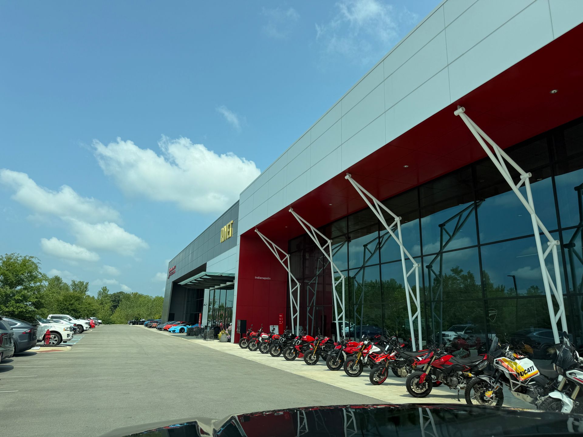Motorcycle dealership exterior with rows of bikes parked outside a red and glass showroom under a blue sky