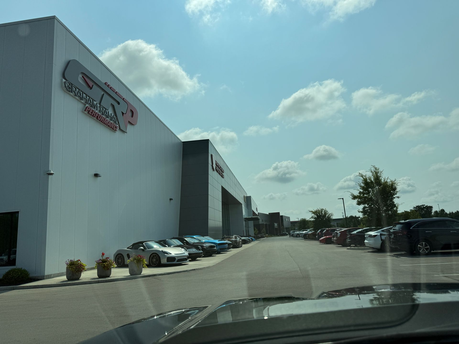 Parking lot beside a large commercial building on a sunny day, with cars lined along the road.