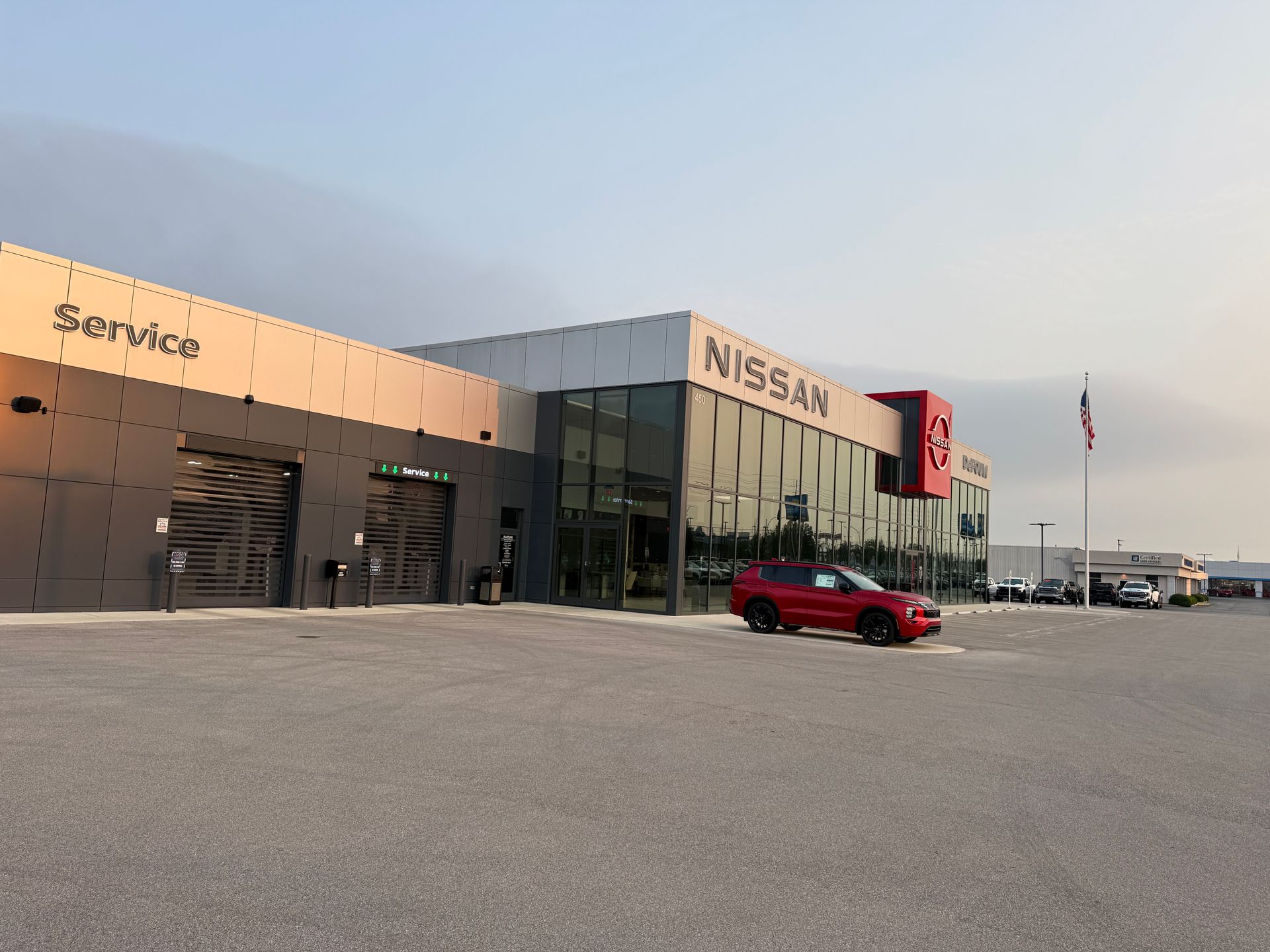 Nissan dealership exterior at sunset with a red car parked in front