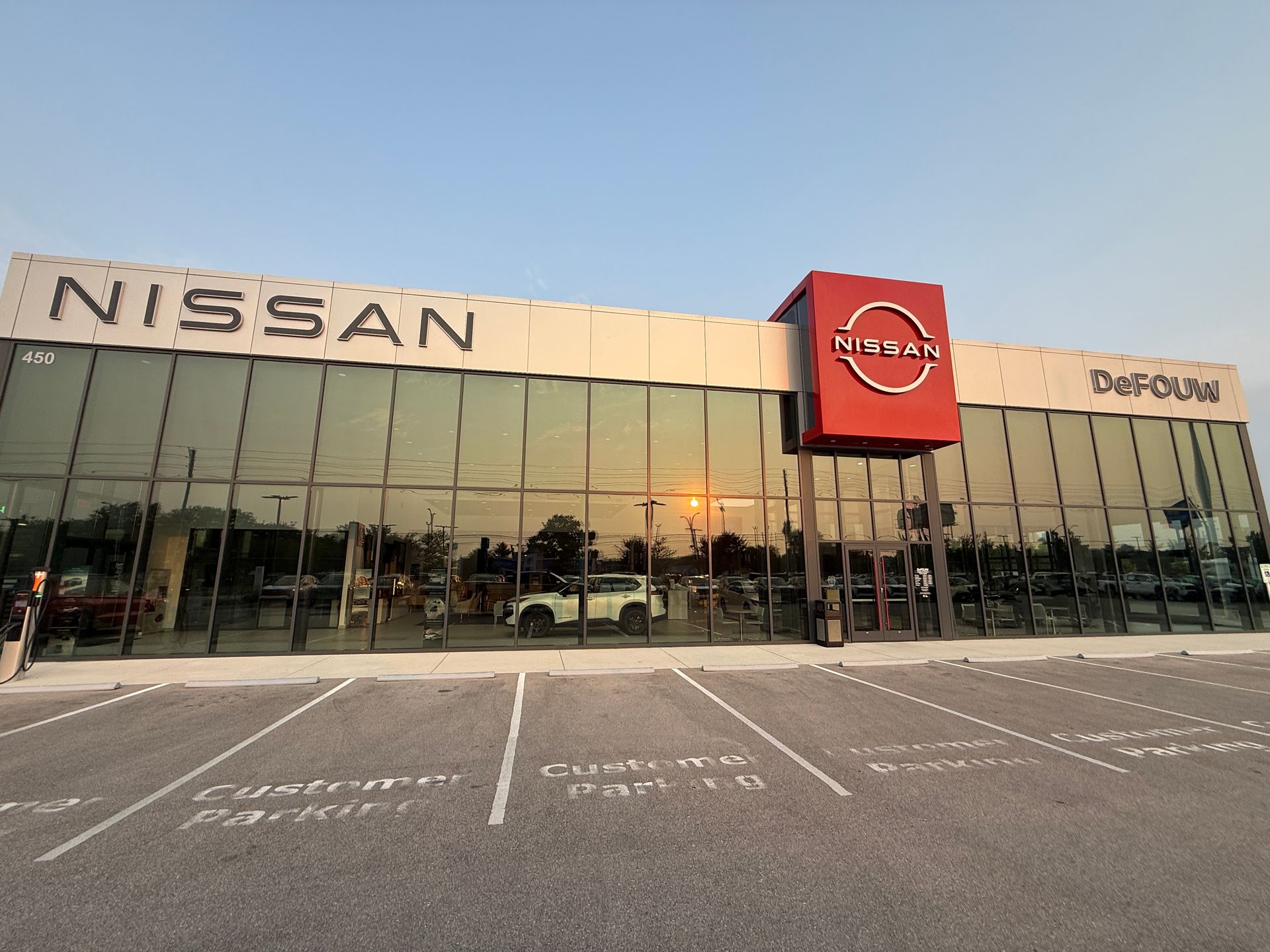 Nissan car dealership storefront with glass facade and parking spaces in front at sunset
