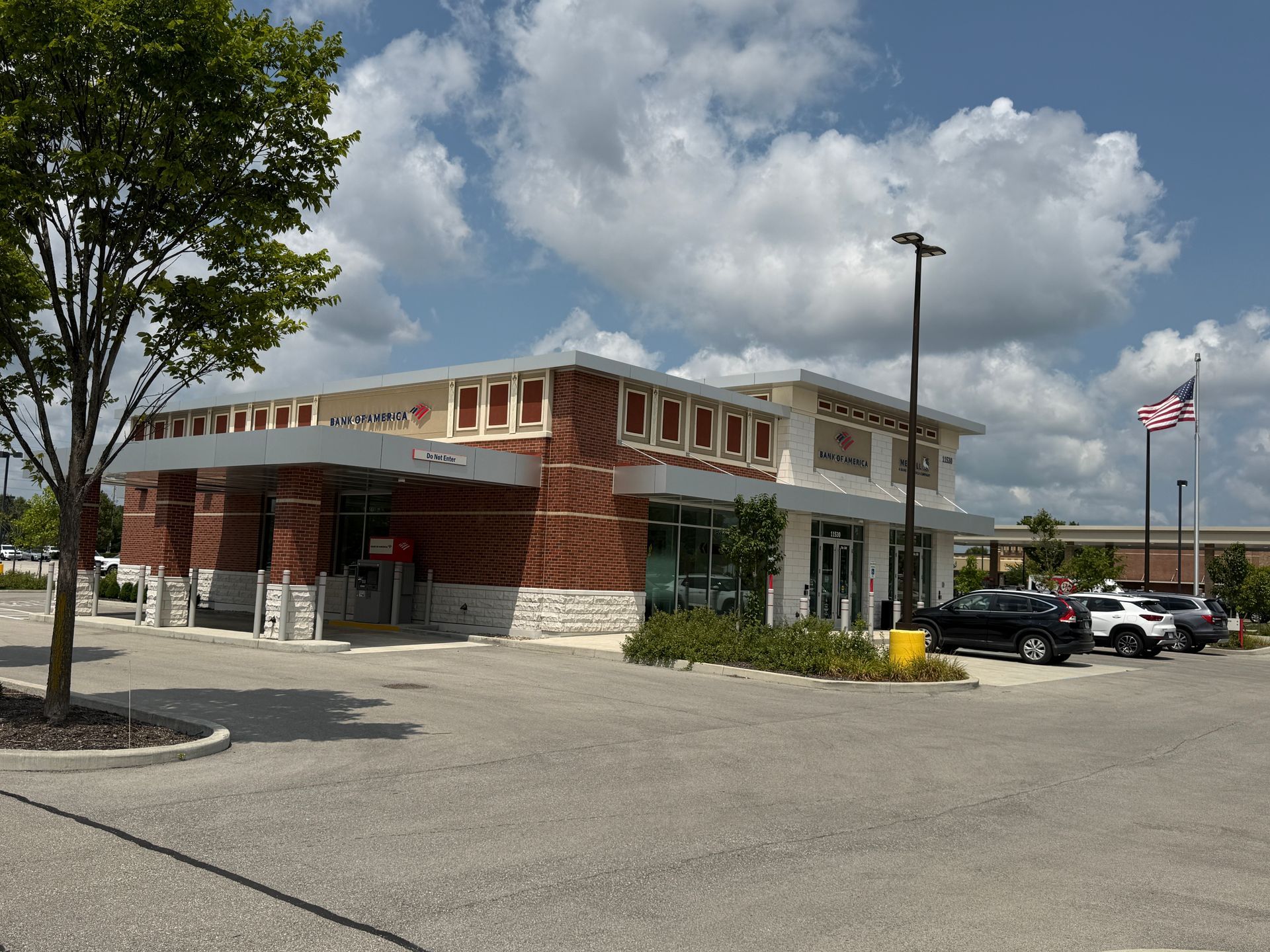 Brick storefront with a drive-thru parking lot and an American flag on a sunny day