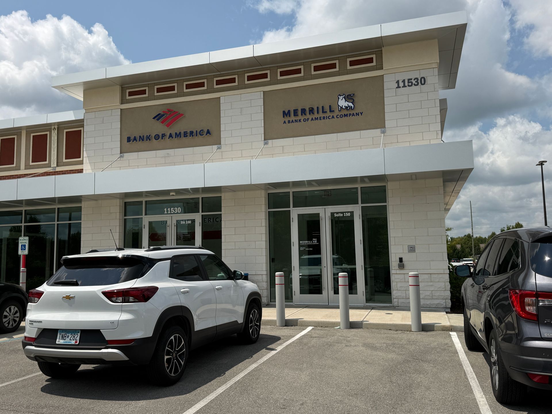 Exterior of a small shopping plaza with parked SUVs under a partly cloudy sky