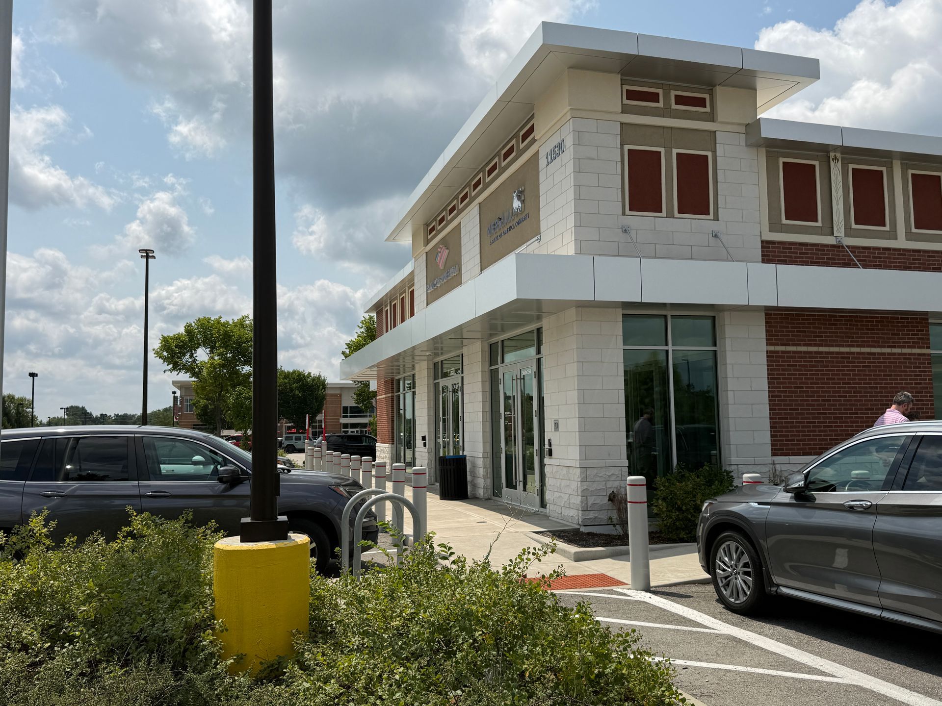 Modern storefront with glass entrance, parked cars, and a yellow bollard in the foreground