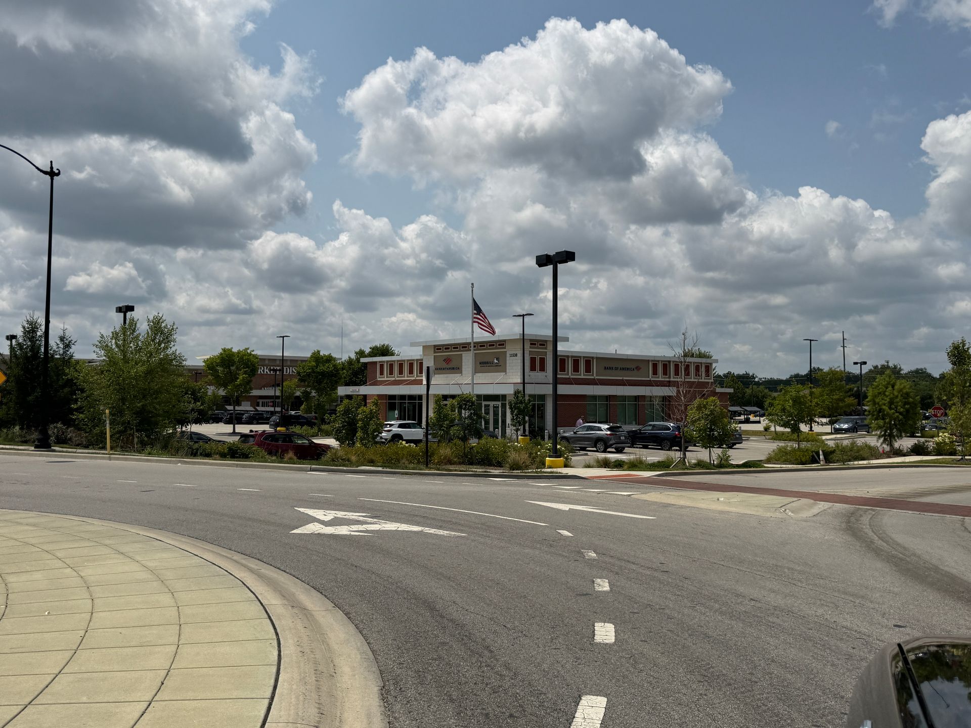 Street scene with a brick building, parking lot, and American flag under cloudy sky