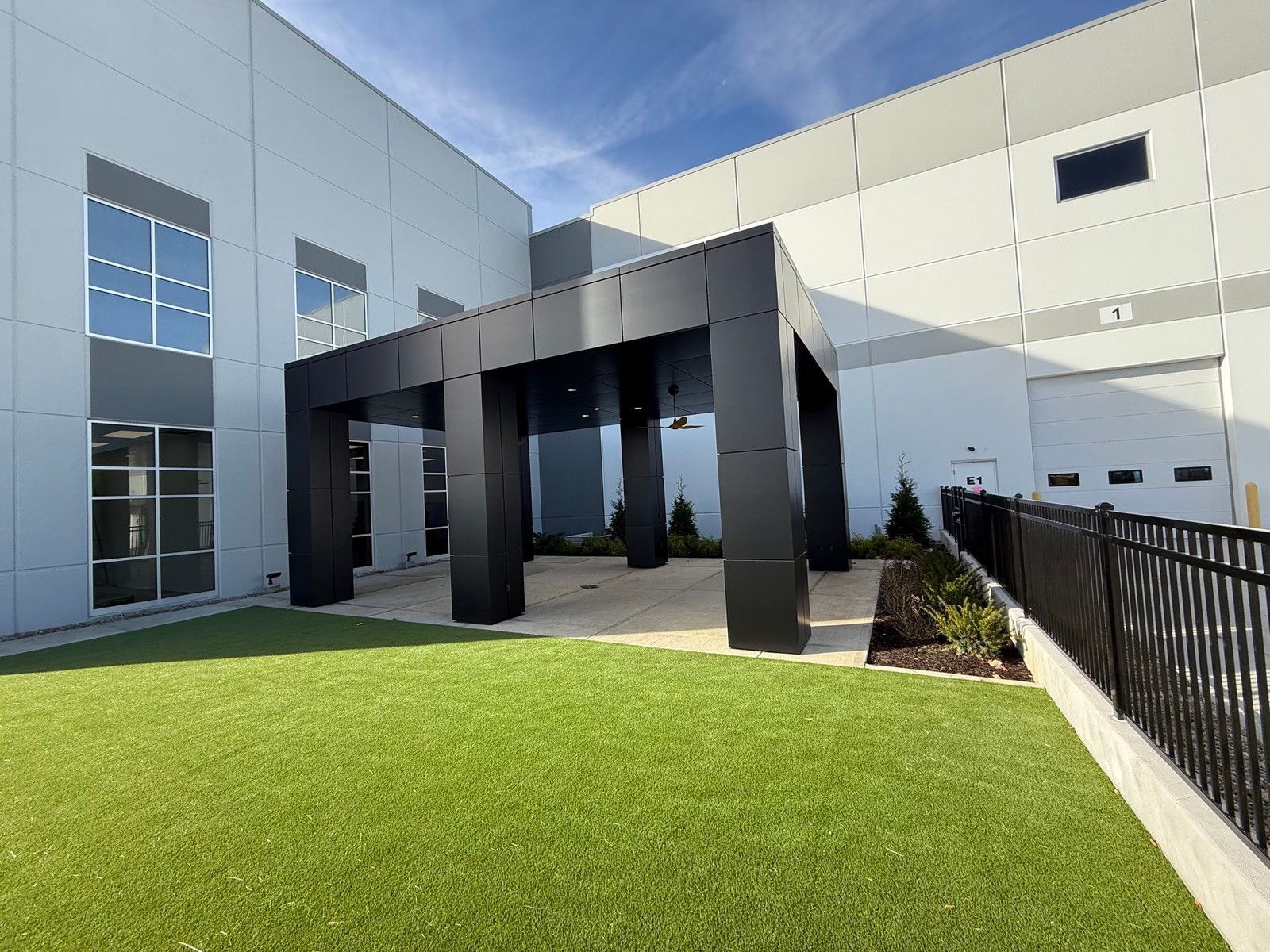 Modern building courtyard with green lawn and a black pergola entrance
