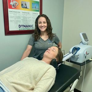 A woman is laying on a table in front of a poster that says dynamic chiropractic