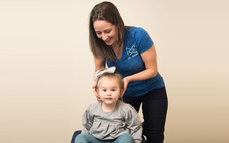 A woman is putting a bow on a little girl 's head.