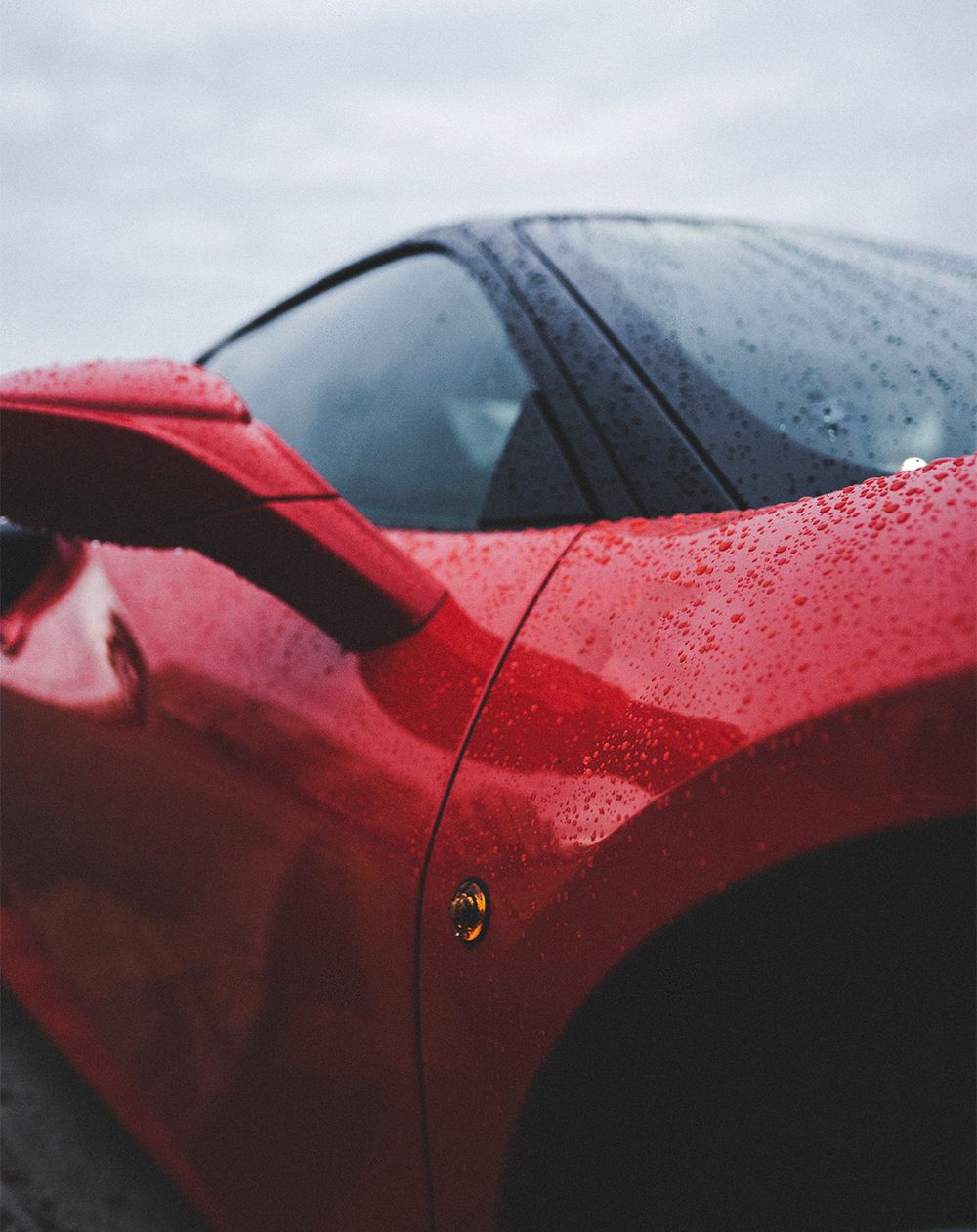 a red sports car is parked on the side of the road in the rain