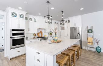 a kitchen with white cabinets , stainless steel appliances , a large island , and wooden stools 
