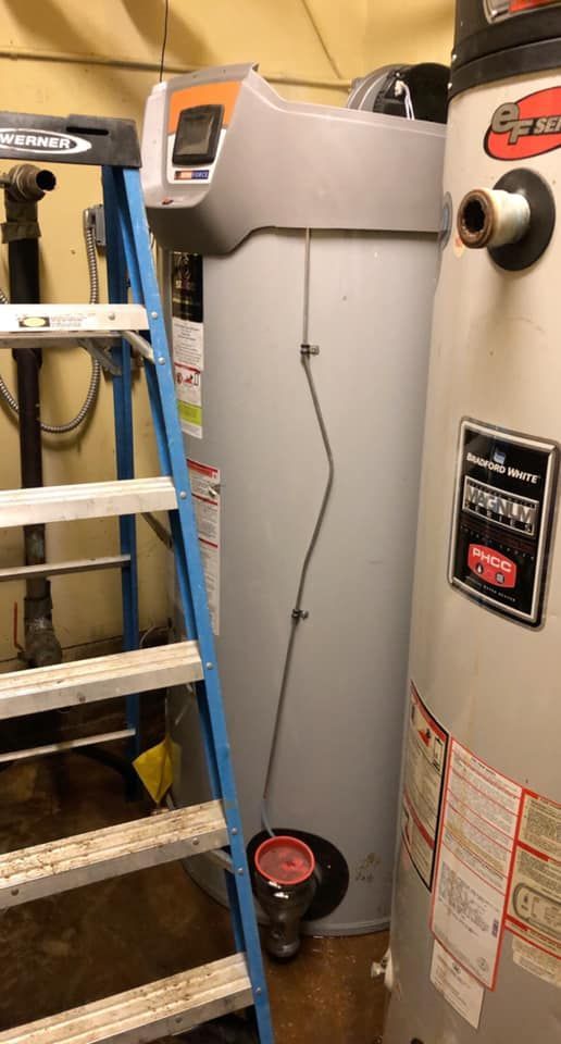 Water heaters next to a blue step ladder in a utility room.