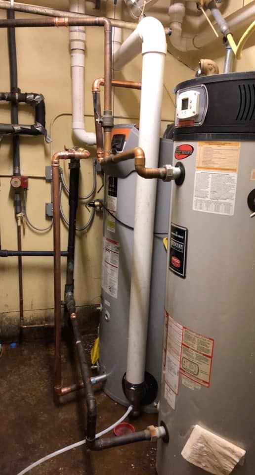 Water heaters and copper pipes in a utility room. White vent pipe.