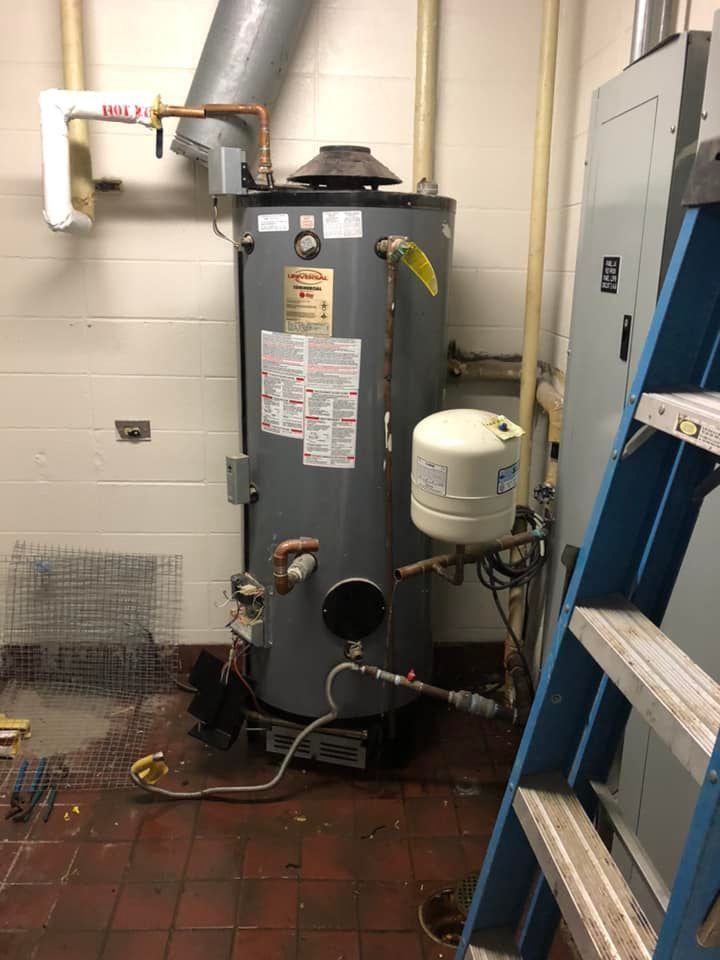 Water heater in a utility room; copper and galvanized pipes, ventilation, and a ladder are also present.