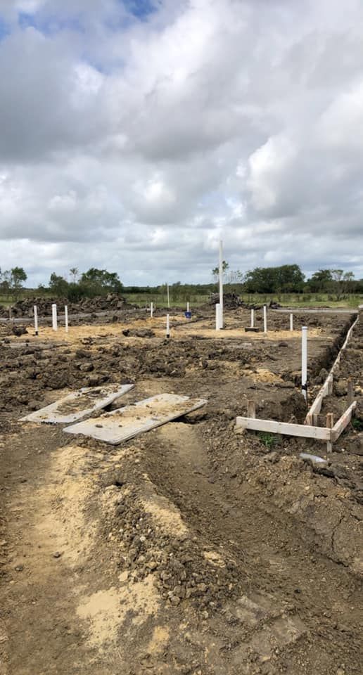 Construction site: foundation pillars and trenching in dirt under cloudy sky.