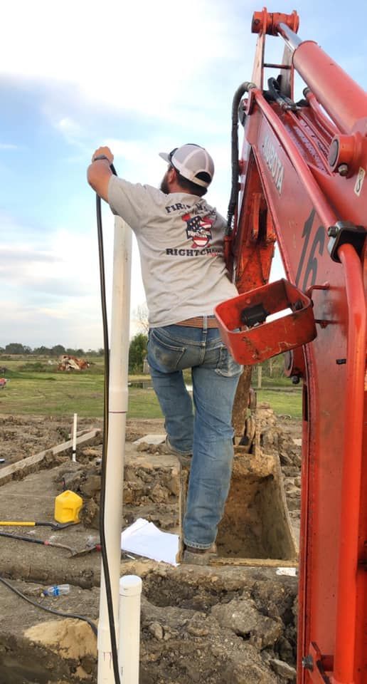Person installing pipe near an excavator; outdoor setting.
