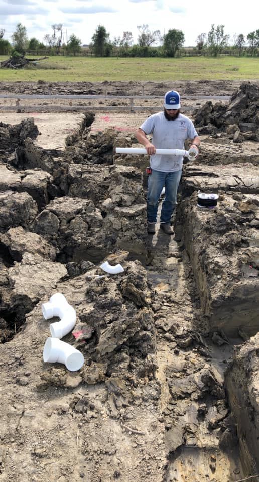 Construction worker in trench, handling PVC pipes. Cloudy day, open field setting.