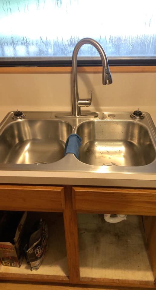 Kitchen sink with stainless steel basin, modern faucet, and open cabinets.