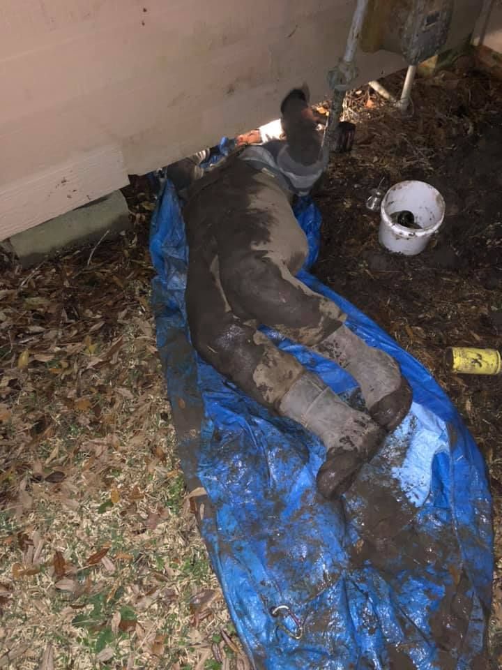 Torso and legs covered in mud on blue tarp. Near a white structure and bucket.