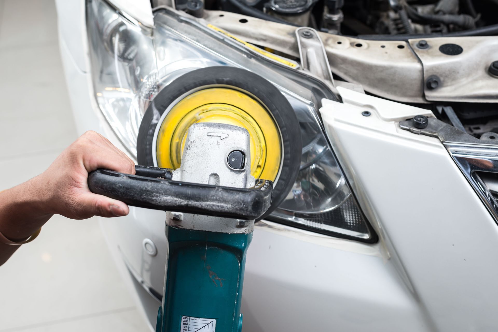 Person polishes car headlight with a buffing tool.
