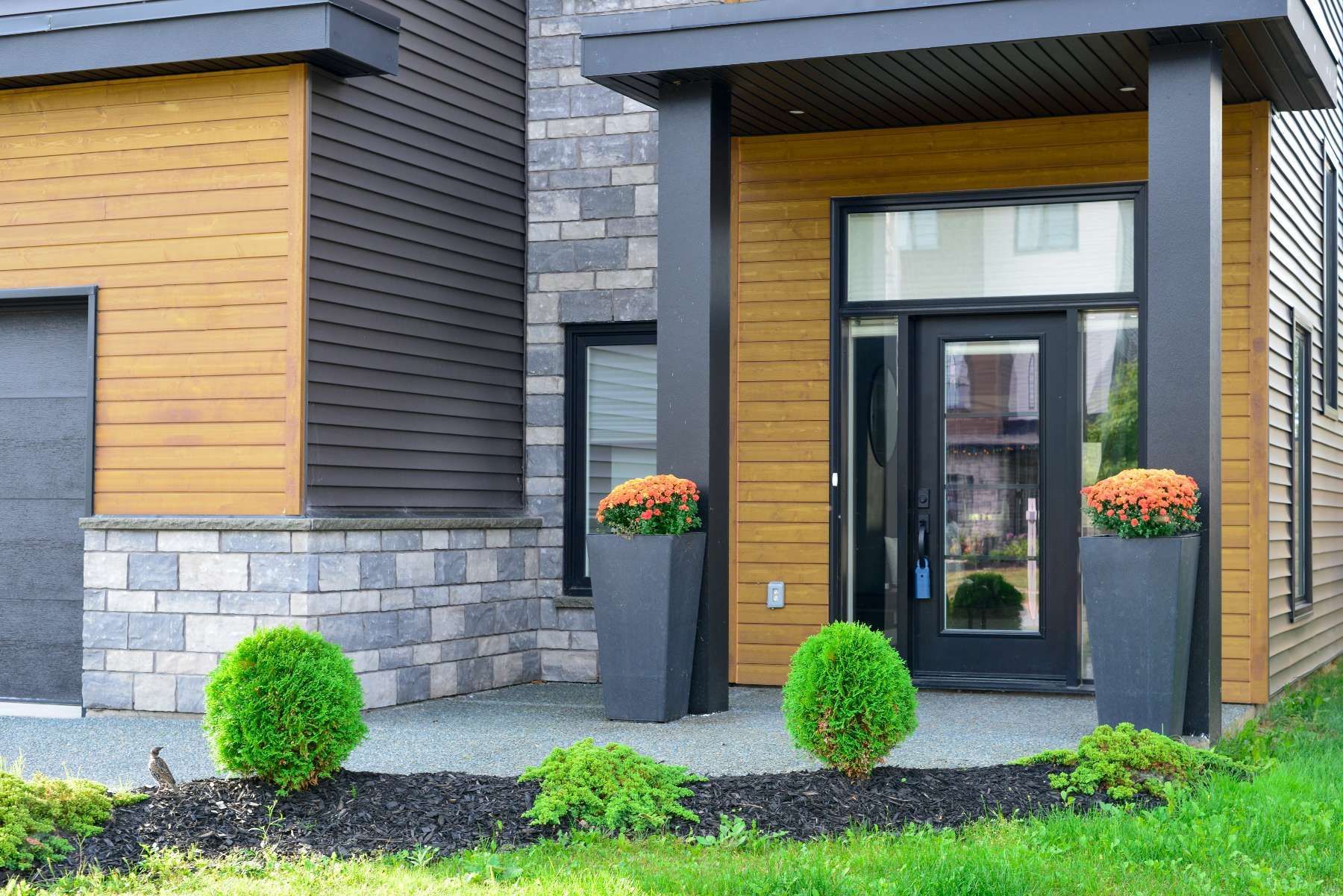 A modern house with a porch and planters in front of it.