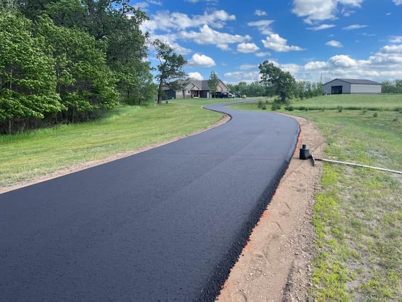 A newly paved road is going through a grassy field.