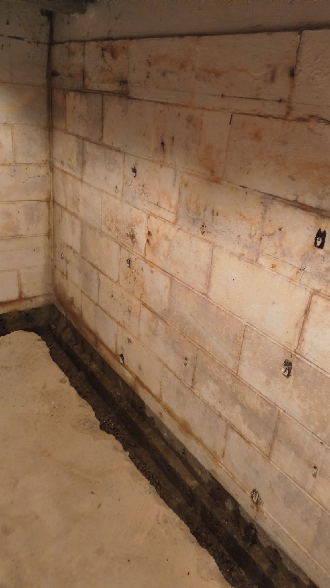 Corner of a basement with concrete block walls; dark drainage channel along the floor.