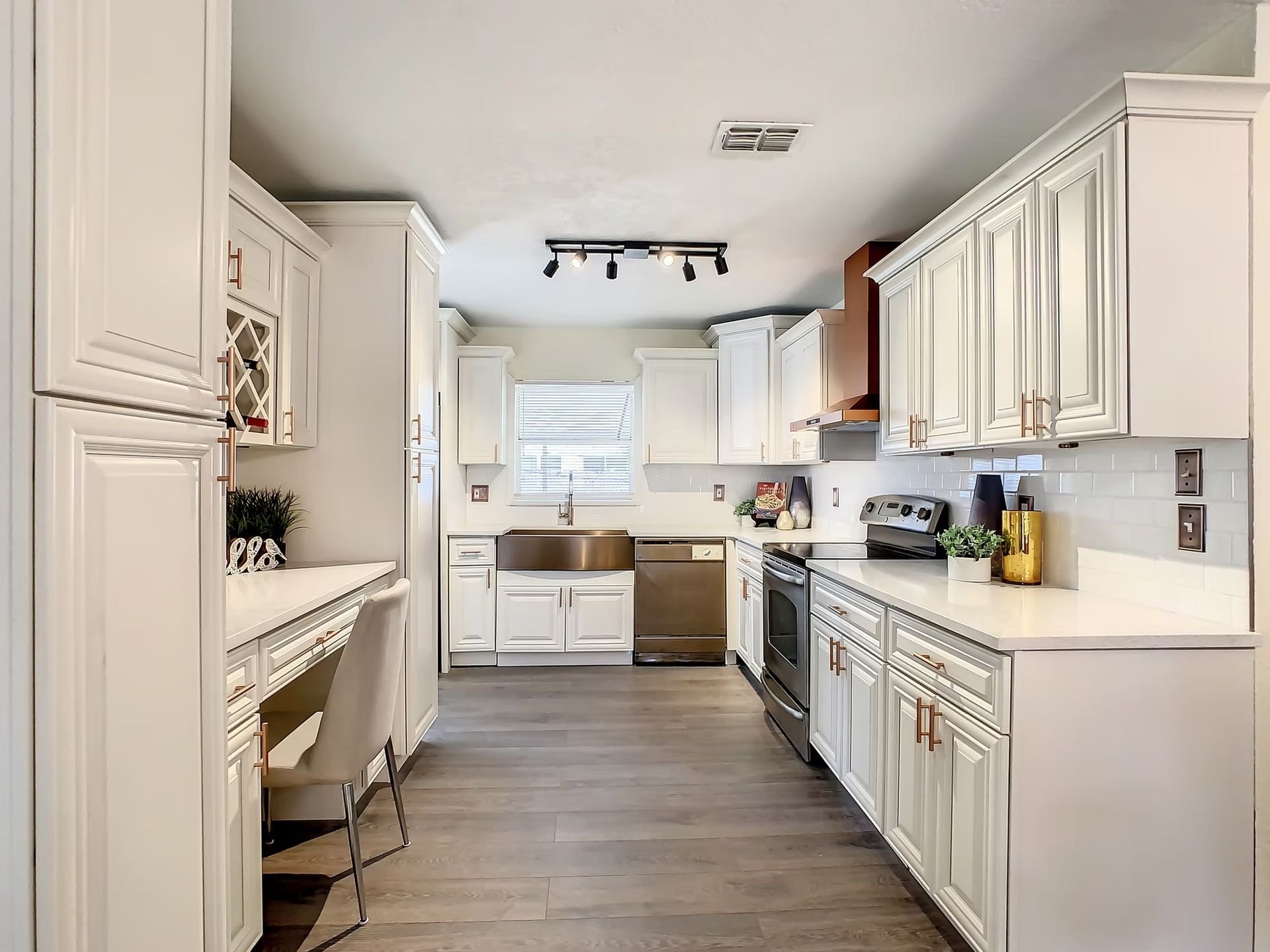 A kitchen with white cabinets, stainless steel appliances, a sink, and a desk.