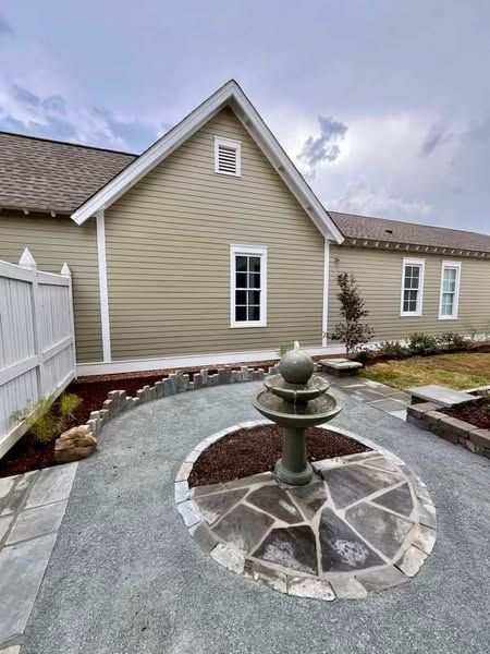 A beige building with white trim and windows, a decorative fountain, and a stone-paved garden.
