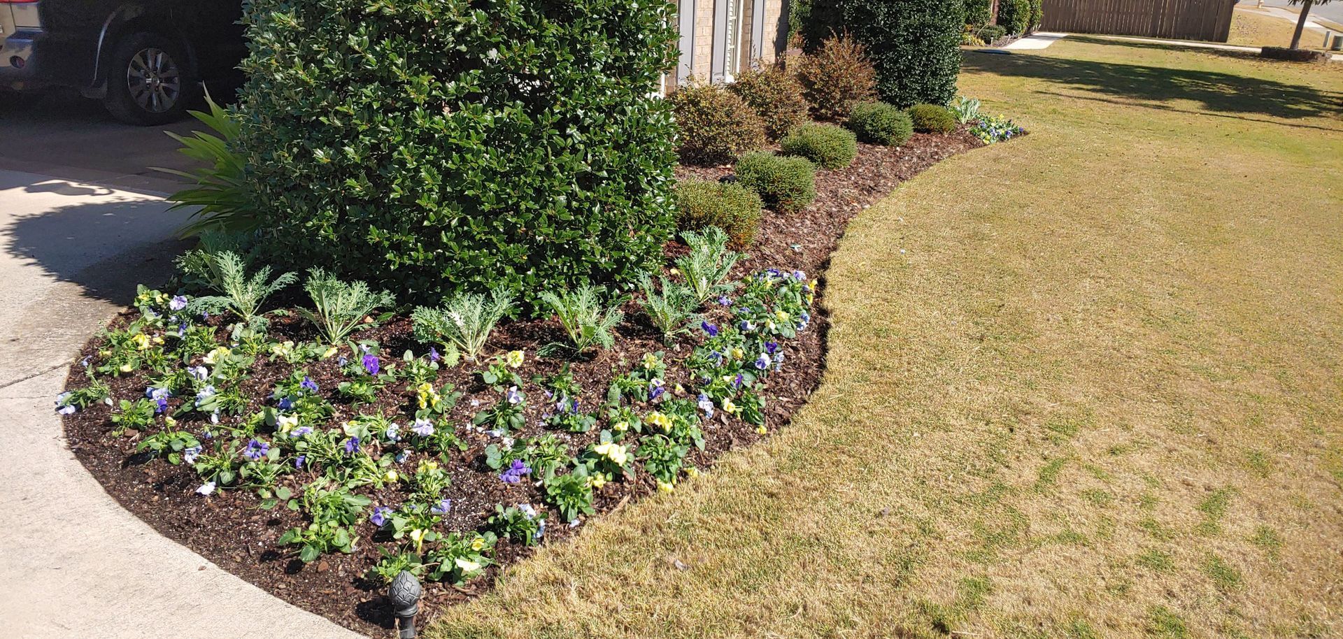 A landscaped garden bed with flowers and shrubs, bordered by a lawn and a sidewalk.